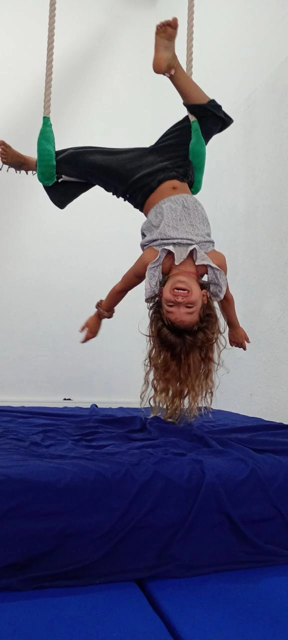 Nena colgada cabeza abajo del trapecio, riéndose